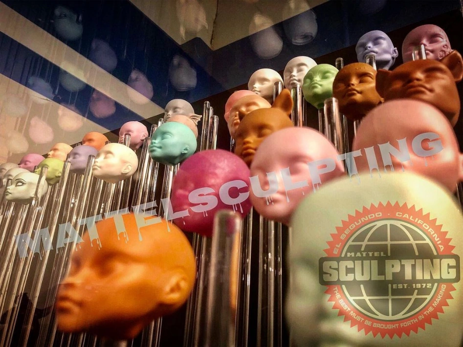 Wall of Mattel doll head sculpts on stainless rods, painted in primer colors